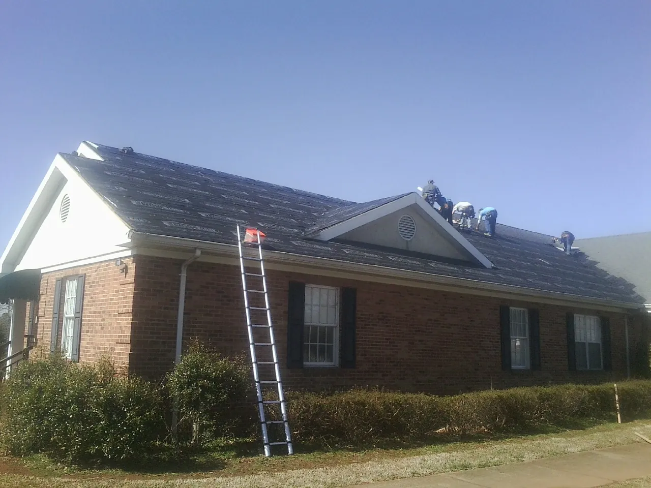 Crew tearing shingles off a brick ranch roof with a ladder set — Metal Roof Repair work by our crew in Thomaston