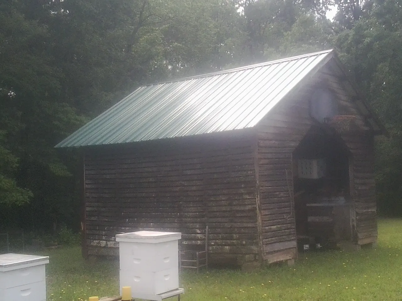 Green metal roof on a weathered barn beside stacked beehives in Thomaston