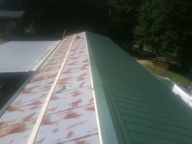 Old rusted panels beside newly installed green metal roofing — Wind Damage Roof Repair by Roofing Brothers in Thomaston