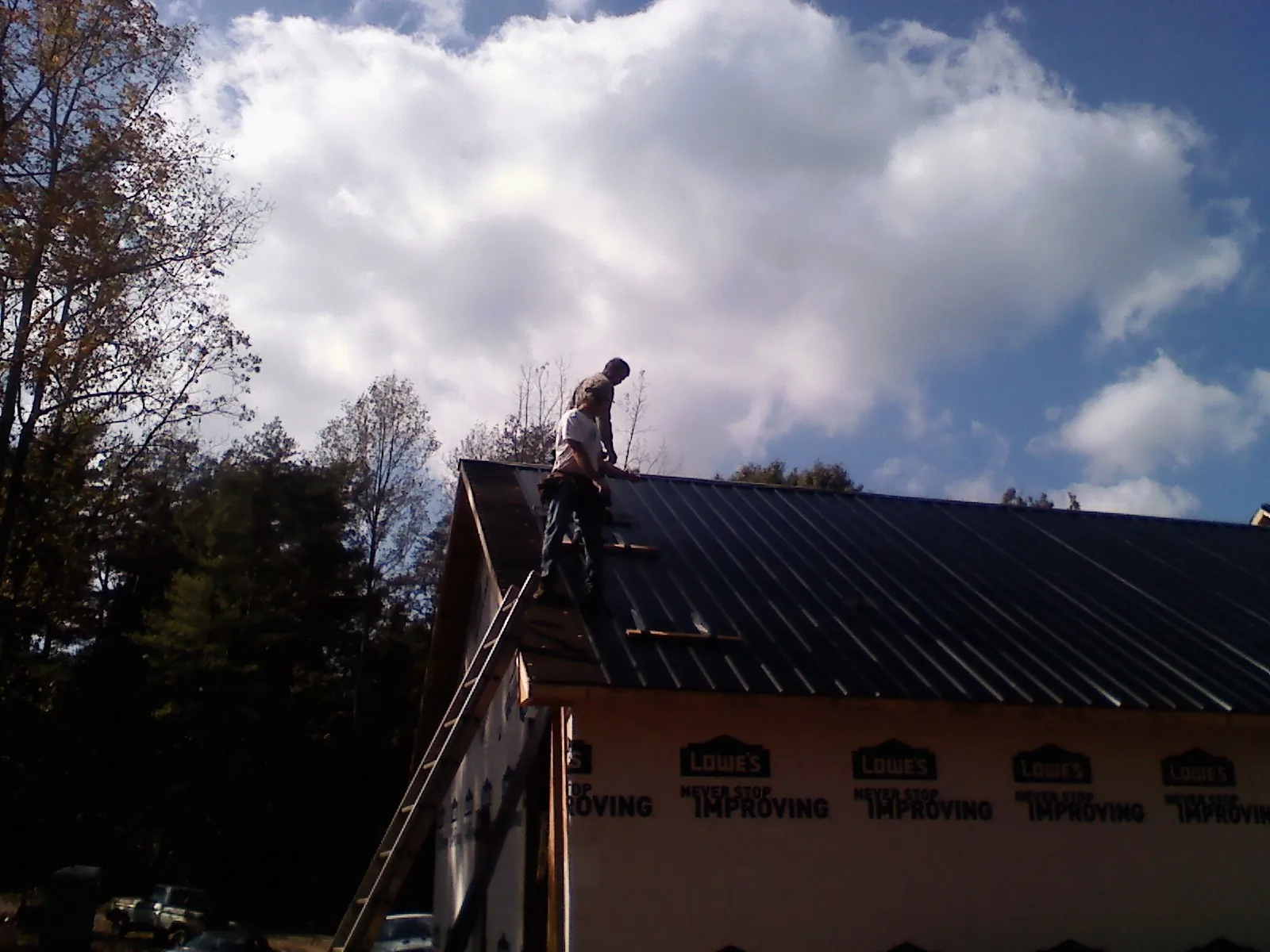 Roofer fastening dark metal panels high against a cloudy sky, from a Roof Inspection job in Thomaston